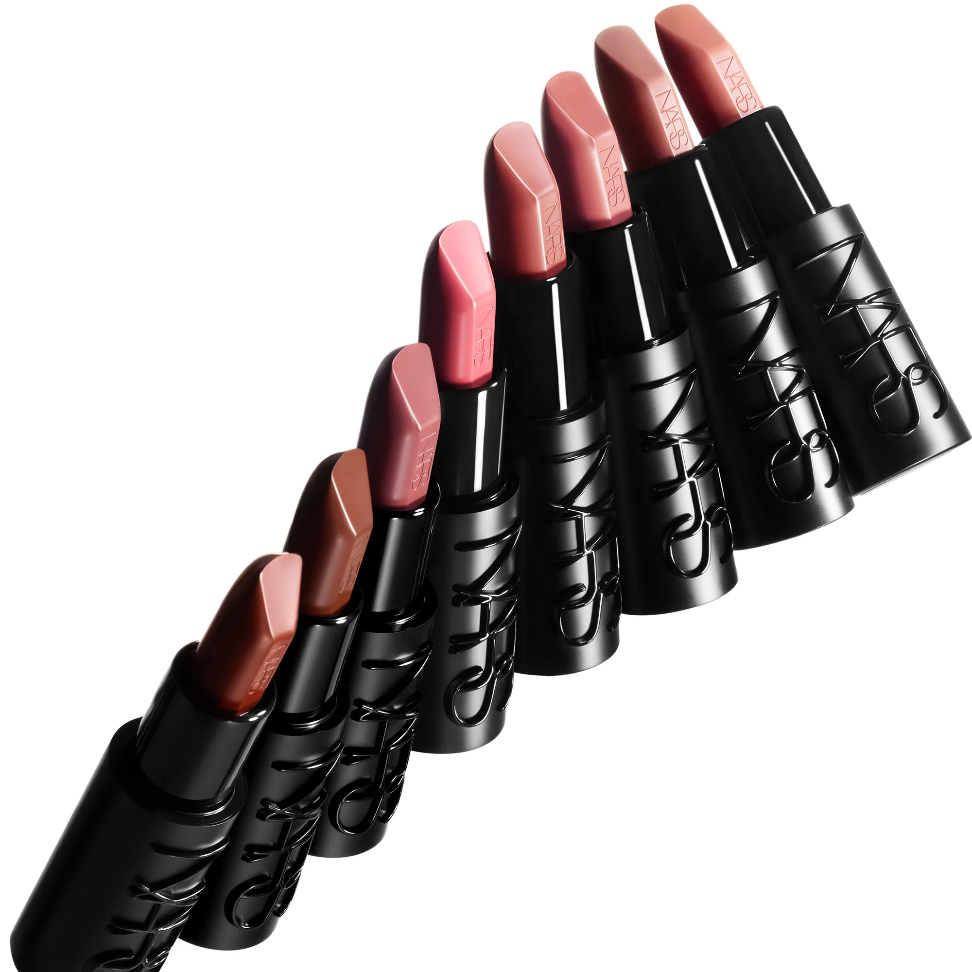 En rekke NARS leppestifter i nude-, rosa- og ferskentoner vises diagonalt mot en lys bakgrunn. De svarte hylsene er merket med den pregede logoen “NARS”, som også er synlig på leppestiftene.