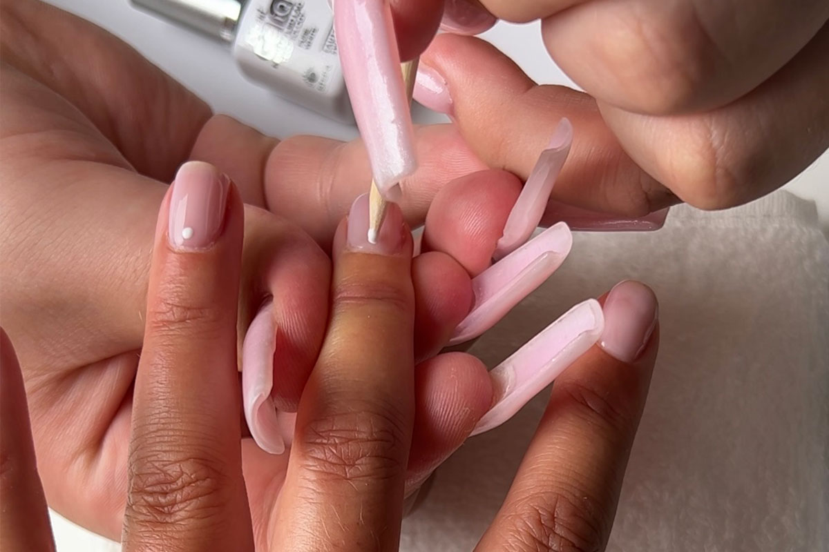 En liten prick av vitt gelpolish appliceras på nageln som en del av nail art-design.