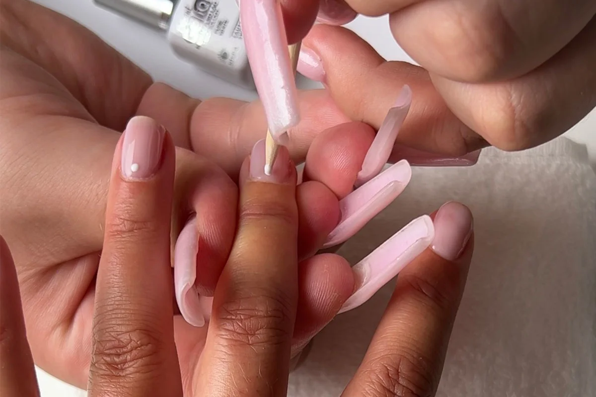 En liten prick av vitt gelpolish appliceras på nageln som en del av nail art-design.