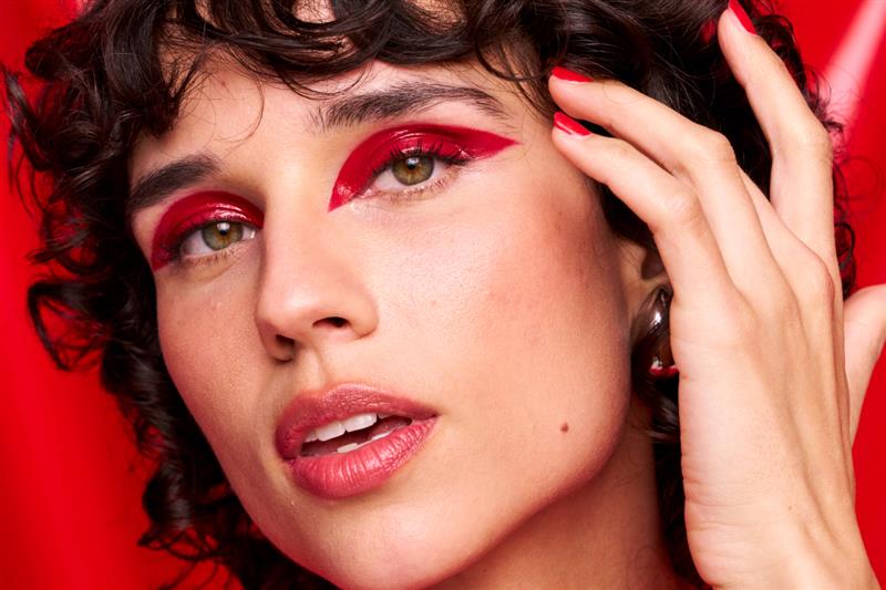 Kvinne med mørkt hår og rød øyenskygge står mot en rød bakgrunn. 