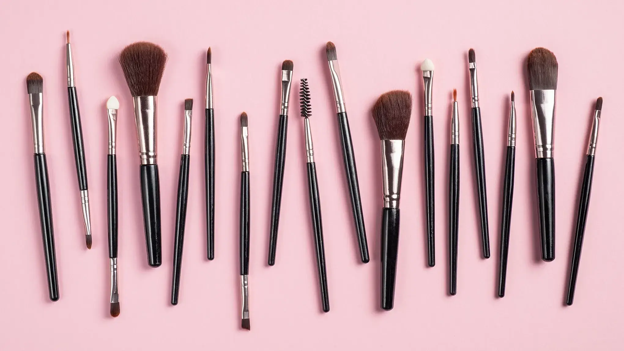 Uppställning av sminkborstar mot en rosa bakgrund.