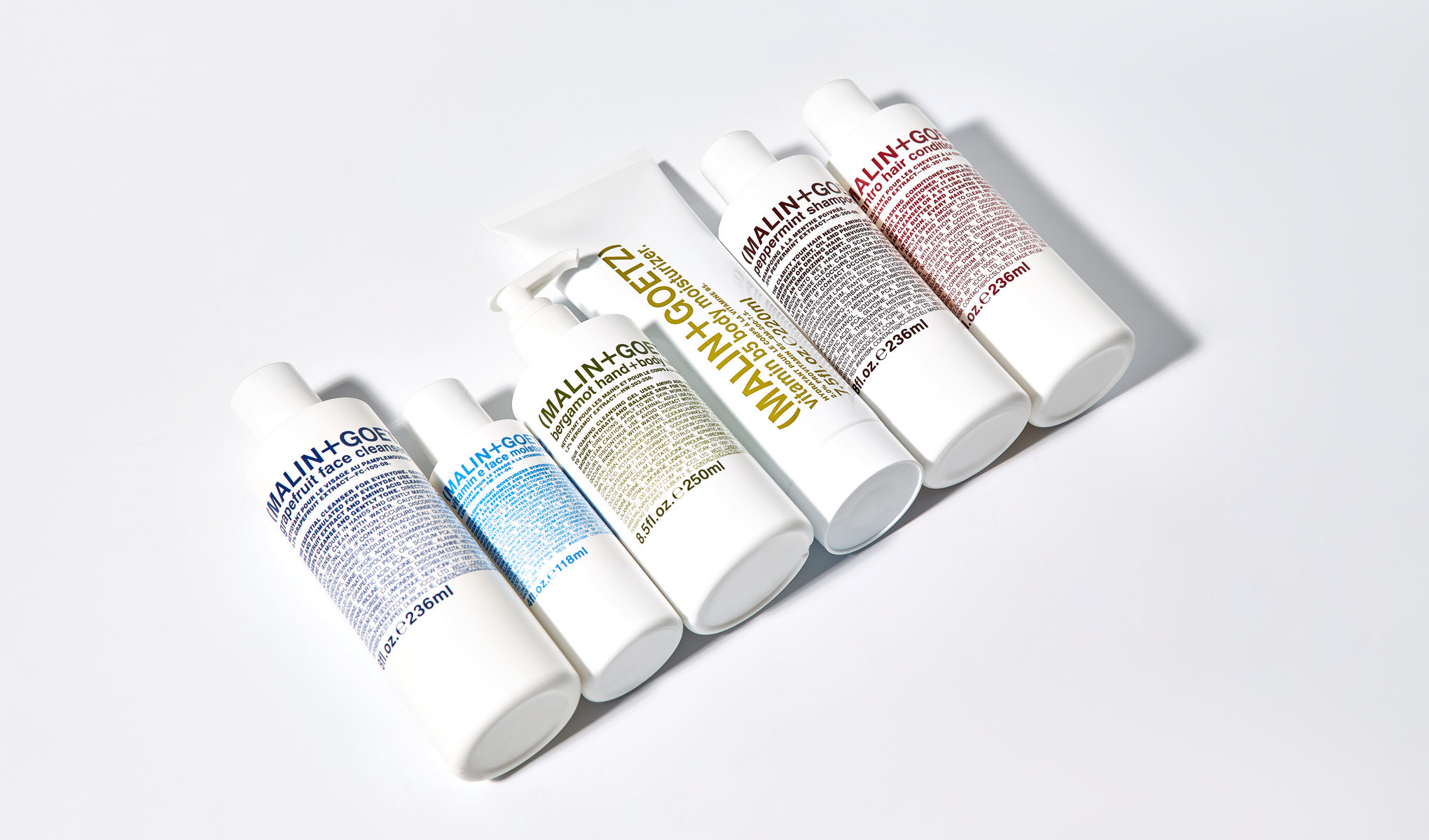 MALIN+GOETZ-ihonhoito- ja hiustenhoitotuotteita valkoisissa pakkauksissa vaaleaa taustaa vasten. Näkyvä teksti sisältää “MALIN+GOETZ”, “grapefruit face cleanser”, “vitamin B5 body moisturizer”, “bergamot hand+body wash”, “peppermint shampoo” ja “cilantro hair conditioner”.