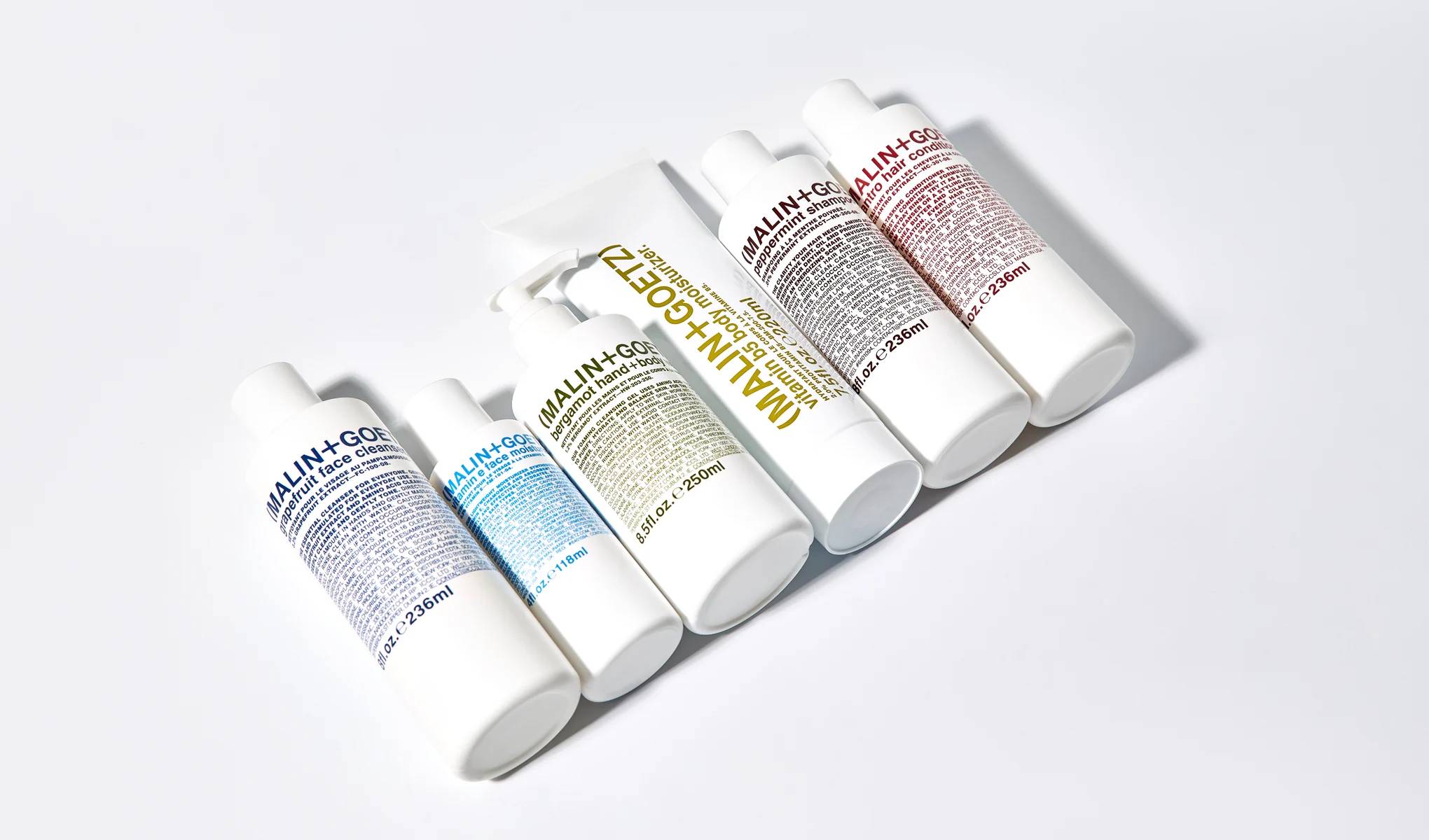 MALIN+GOETZ hudvårds- och hårvårdsprodukter i vita förpackningar arrangerade mot ljus bakgrund. Synlig text inkluderar “MALIN+GOETZ”, “grapefruit face cleanser”, “vitamin B5 body moisturizer”, “bergamot hand+body wash”, “peppermint shampoo” och “cilantro hair conditioner”.