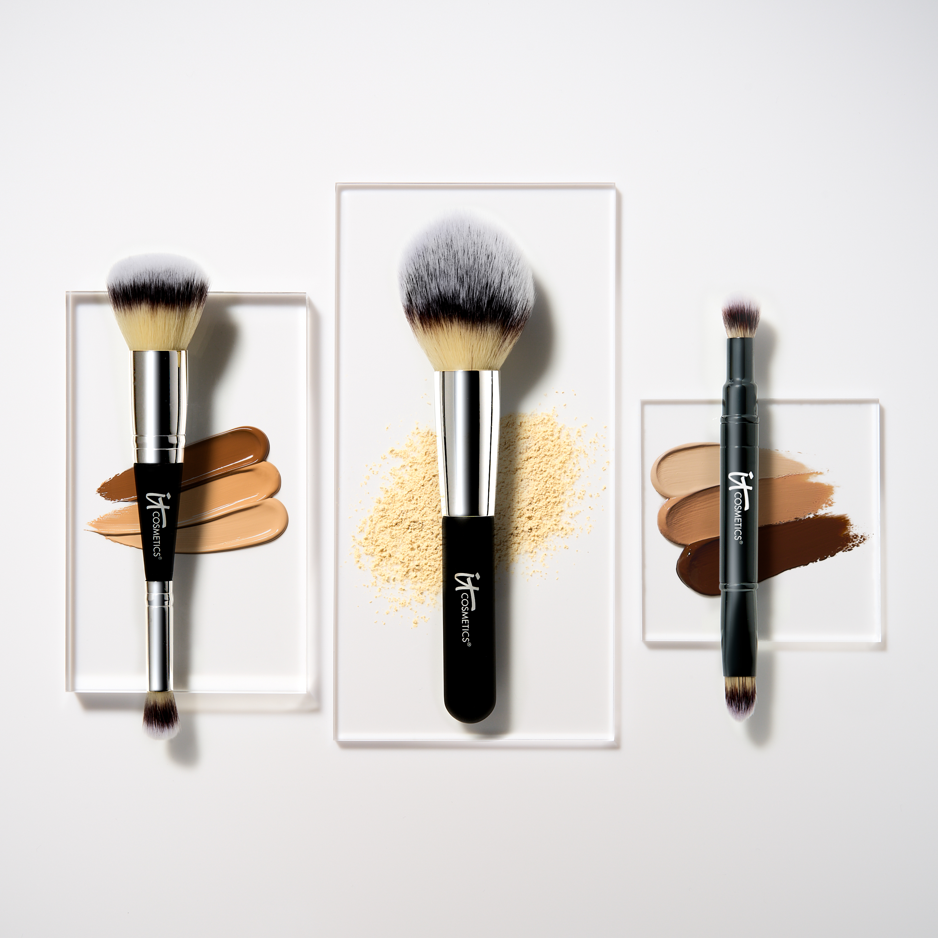 Kolme IT Cosmeticsin meikkisivellintä valkoisella taustalla. Vasemmanpuoleisen siveltimen vieressä on kolme erisävyistä nestemäistä meikkivoidetta, keskimmäisen siveltimen vieressä on irtopuuteri ja oikeanpuoleisen siveltimen vieressä on kolme erisävyistä voidemaskia.