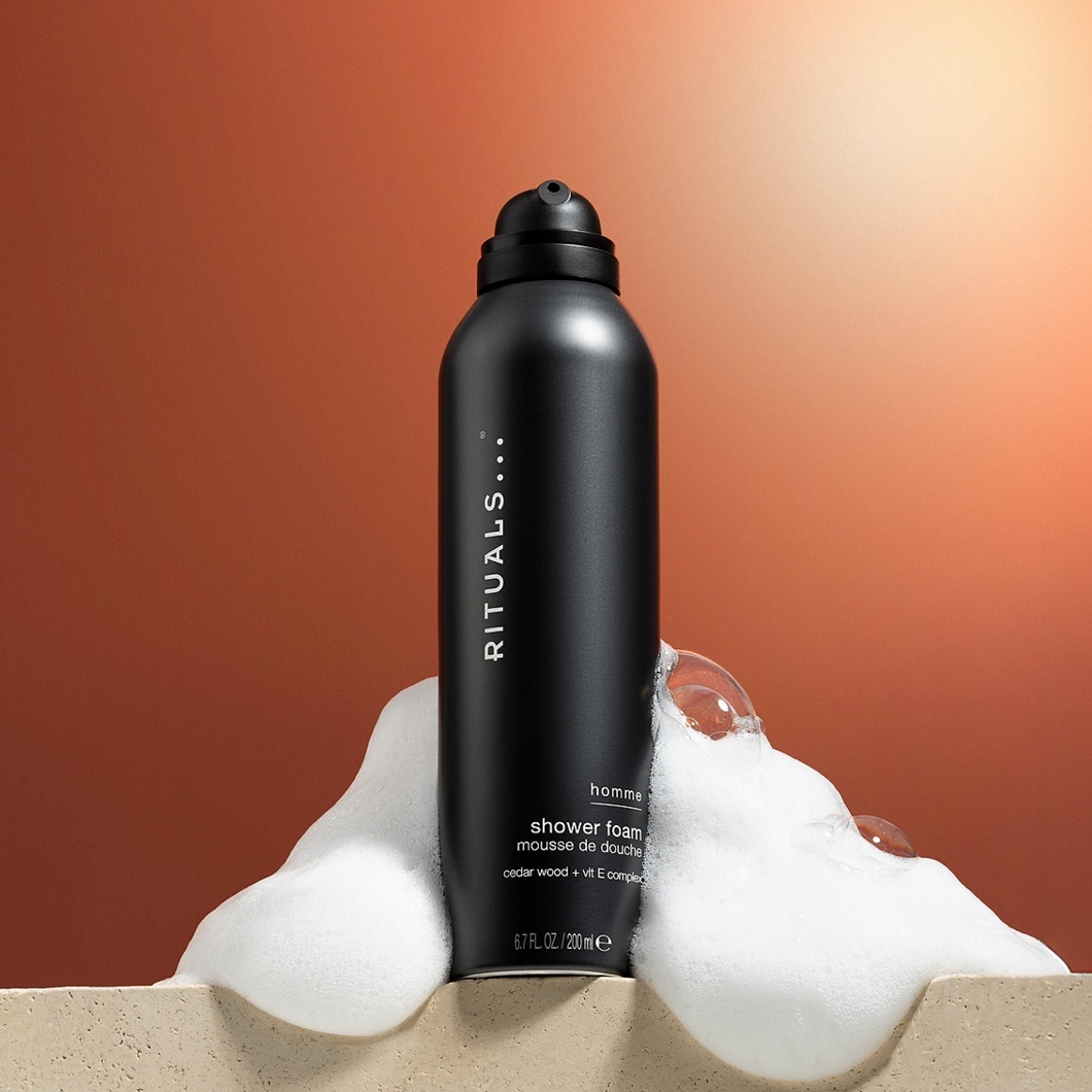 Rituals Homme Shower Foam duschskum (200 ml) med cederträ och vitamin E-komplex, omgivet av vitt skum.