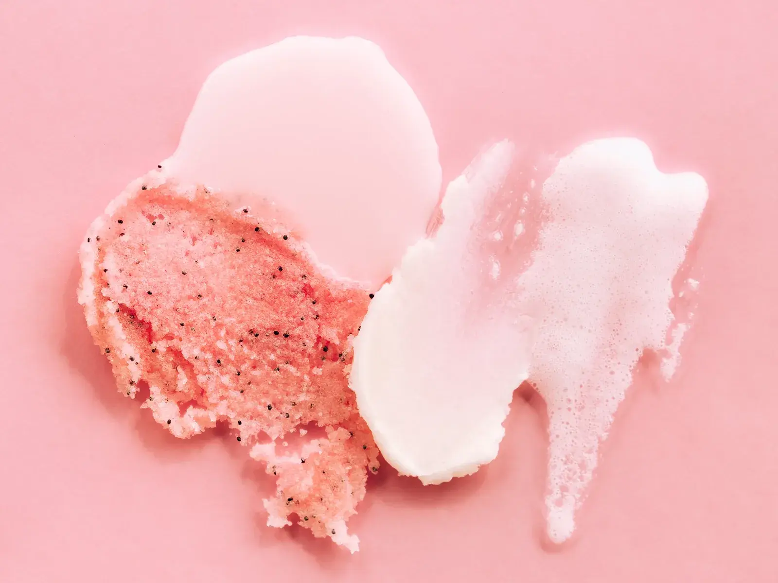 Olika konsistenser av ansiktspeeling, inklusive gel, skrubb och skum, i rosa nyanser på en rosa bakgrund.