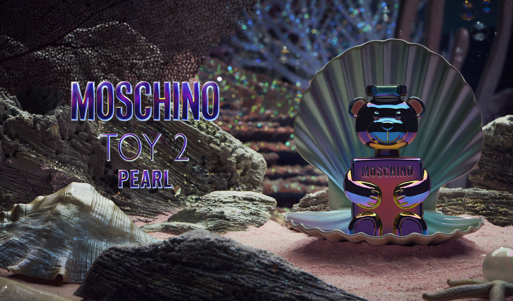En parfymeflaske fra Moschino, formet som en skimrende bjørn, plassert i et stort skjell under vann. Bakgrunnen er dekorert med undervannsplanter, koraller og steiner. Teksten på bildet lyder «Moschino Toy 2 Pearl».