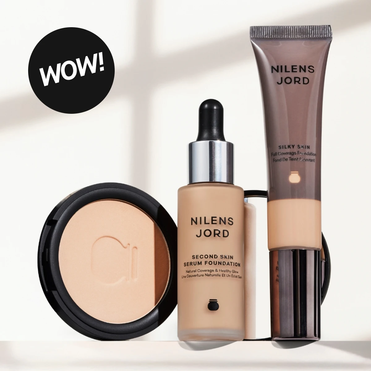 Nilens Jord sminke på lys bakgrunn: Silky Skin foundation, Second Skin Serum Foundation og pudder, med «WOW!»-markering.