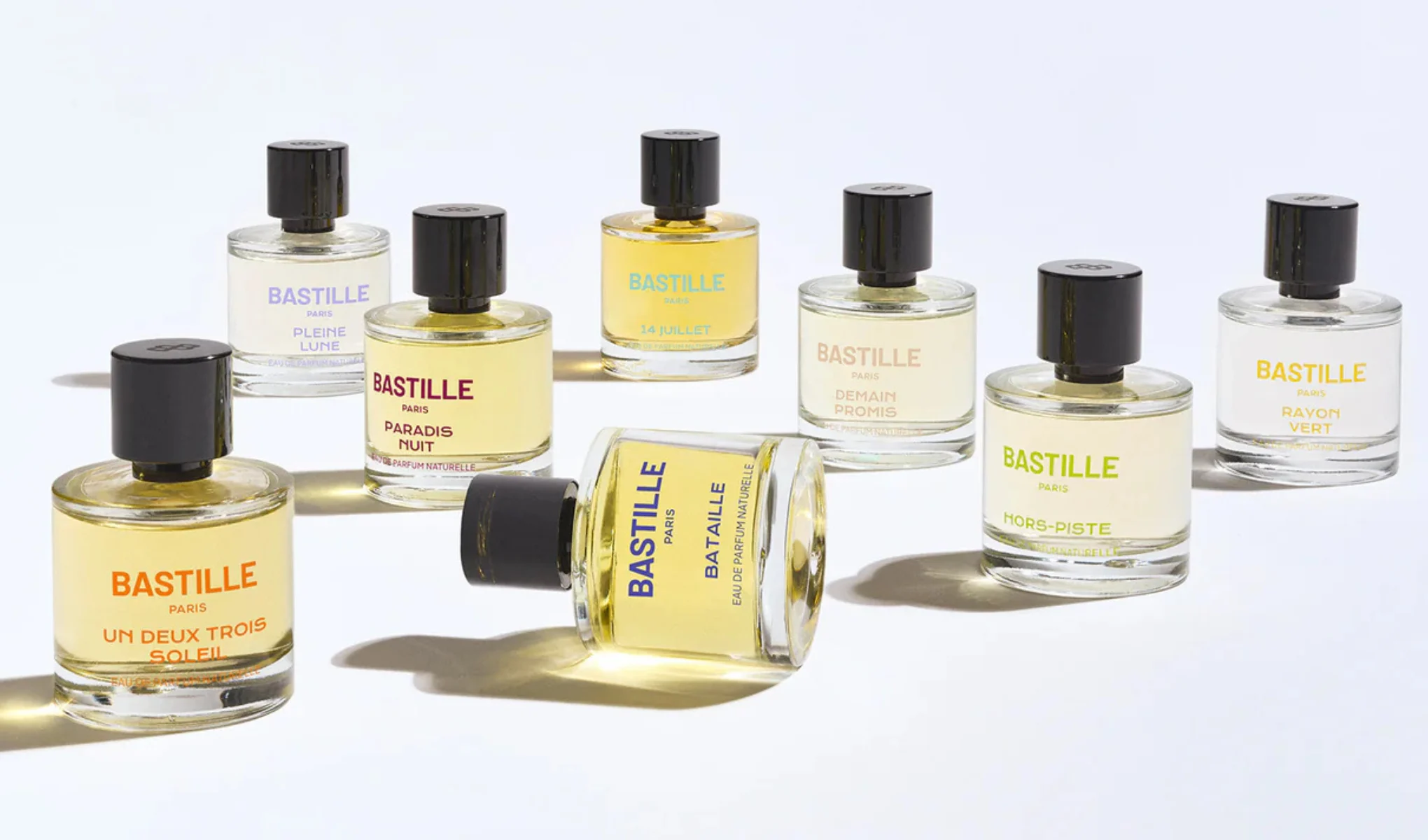 Produktbilde med flere Bastille Paris-parfymer i glassflasker med svarte korker mot lys bakgrunn. Synlige duftnavn inkluderer “Pleine Lune”, “Paradis Nuit”, “14 Juillet”, “Demain Promis”, “Hors-Piste”, “Rayon Vert”, “Un Deux Trois Soleil” og “Bataille”.