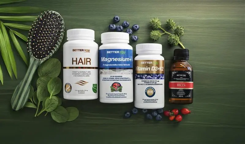 Flatlay med kosttillskott från Better You på grön bakgrund, inklusive burkar märkta “HAIR”, “Magnesium+” och “Vitamin D3+K2” samt en flaska “RICIN”. Produkterna omges av hårborste, blad, blåbär och växter som förstärker en naturlig hår- och hälsovårdskänsla.