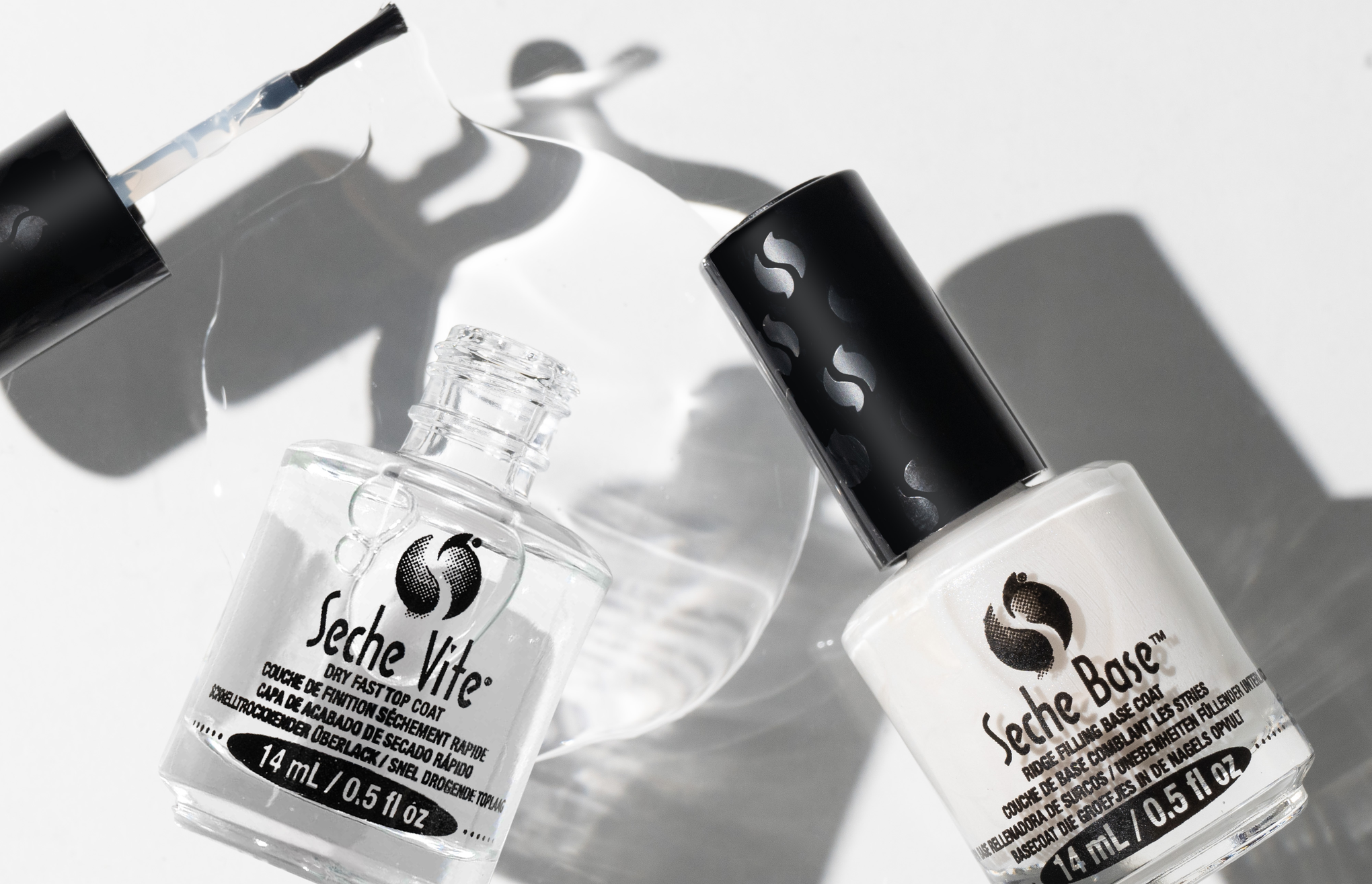 Två nagellacksflaskor från märket Seche, en klar top coat och en vit base coat, på en vit bakgrund.