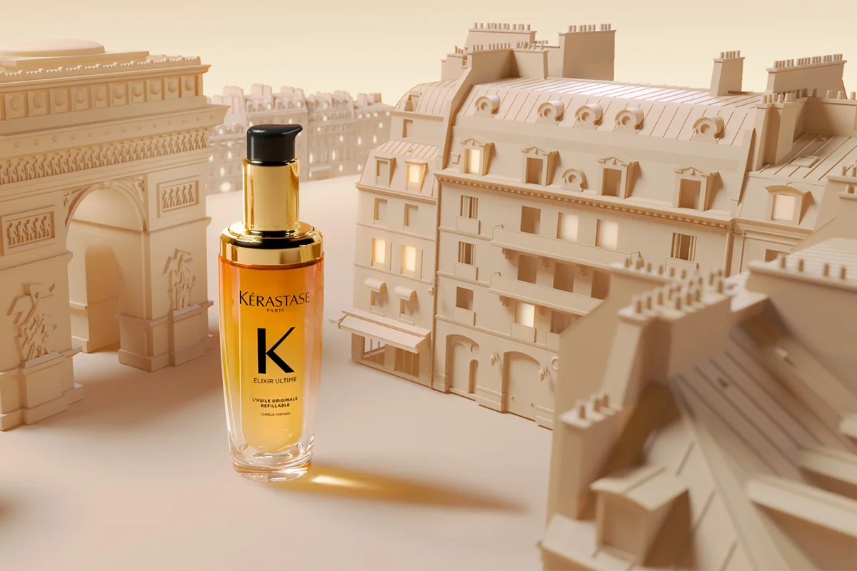 En flaske med Kérastase Elixir Ultime plassert foran en stilisert bakgrunn av Paris. Bakgrunnen består av Triumfbuen og klassiske parisiske bygninger, alle i beige nyanser.