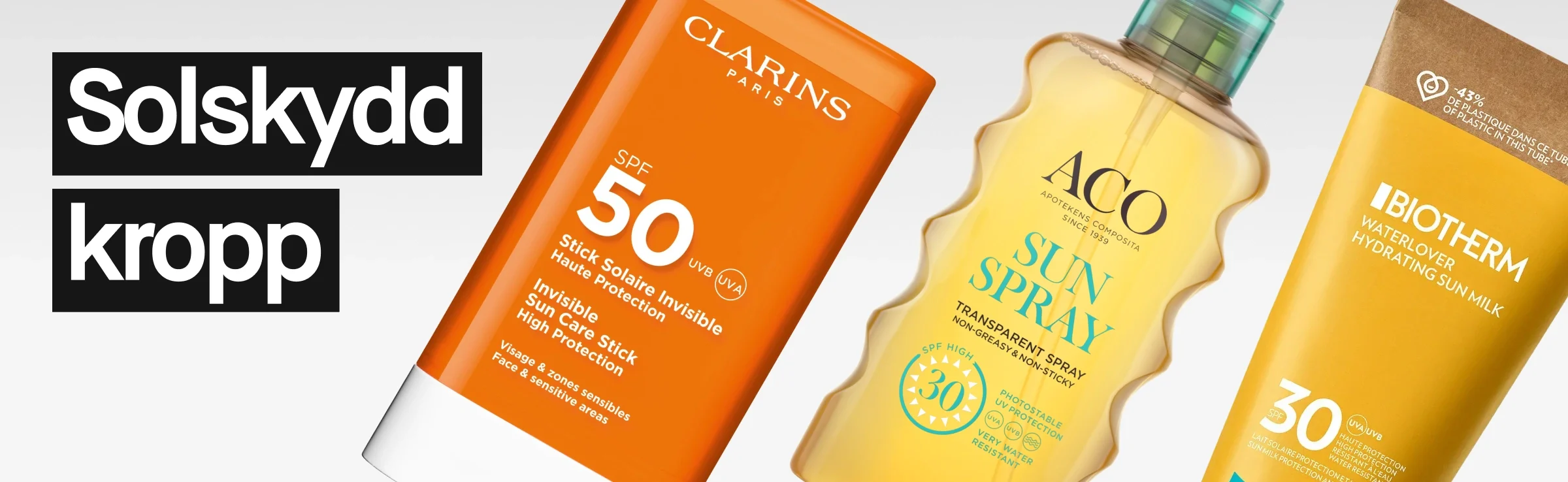 Kolme vartalon aurinkosuojatuotetta vaaleaa taustaa vasten. Vasemmalla teksti “Solbeskyttelse kropp” valkoisella mustalla taustalla. Oikealla näkyy oranssi Clarins SPF 50 -puikko, keltainen Biotherm Waterlover Hydrating Sun Milk SPF 30 -tuubi ja oranssi Lancaster SPF 30 -pumppupullo.