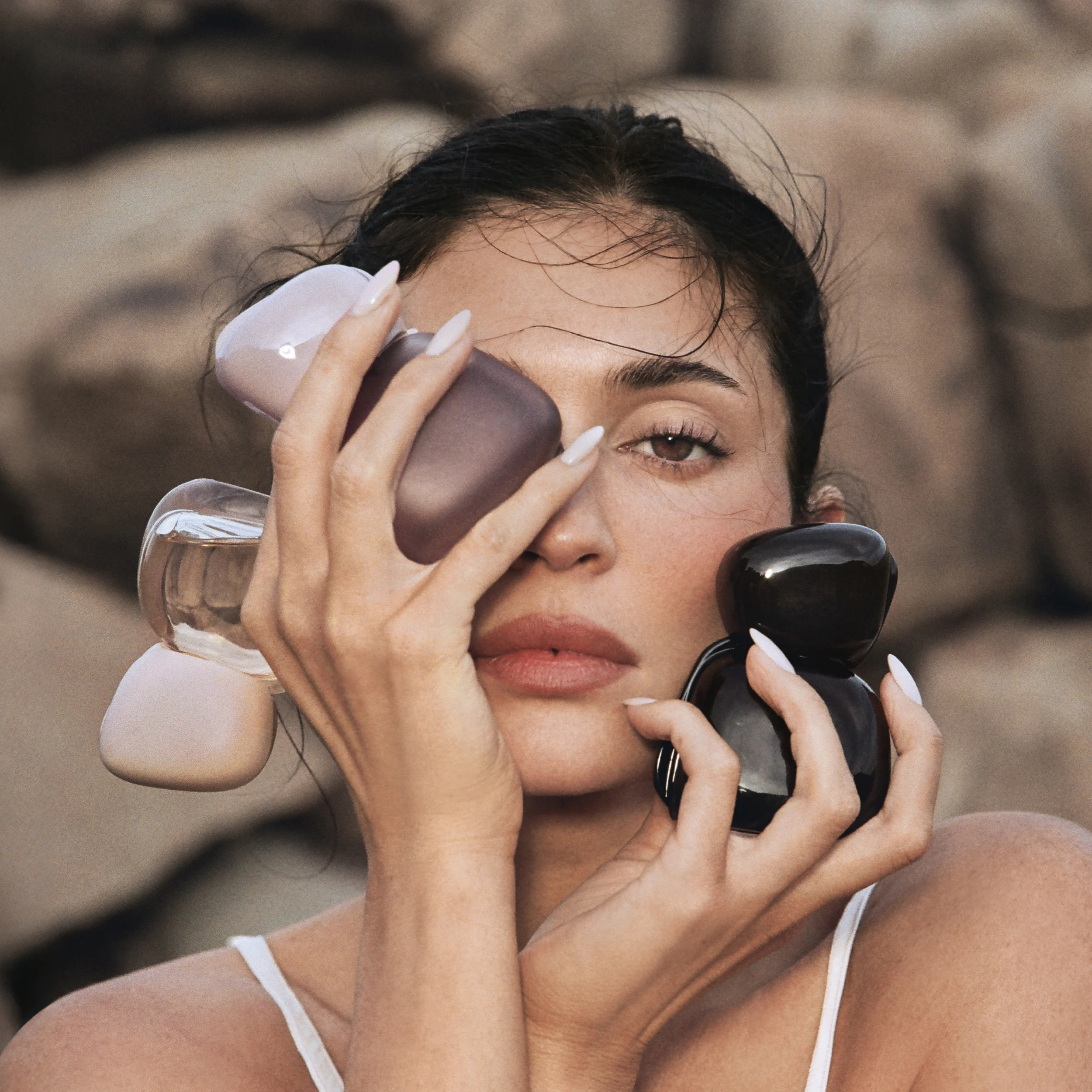 Kvinna håller tre Kylie Cosmetics Mood Stones-parfymflaskor framför ansiktet.