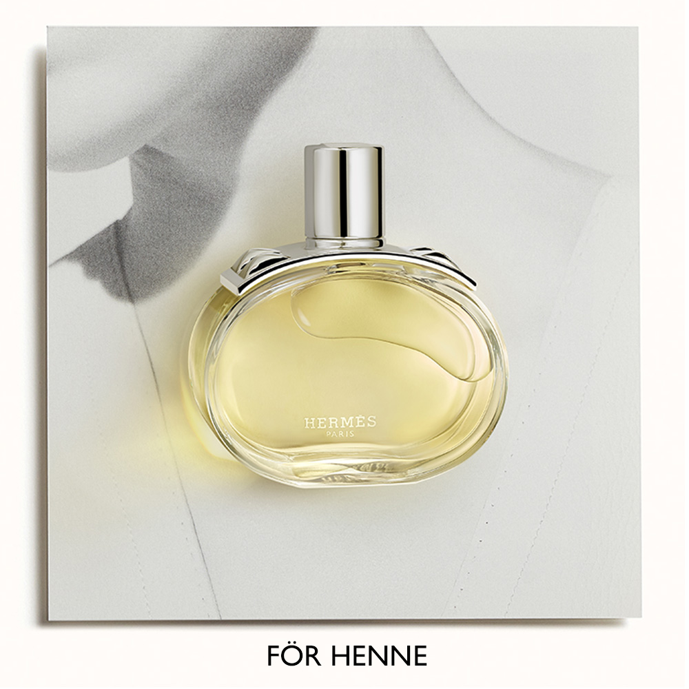 Parfymflaska från Hermès, med en ljusgul vätska, placerad framför en svartvit bild av en kvinnas överkropp. Texten "FÖR HENNE" syns längst ner.