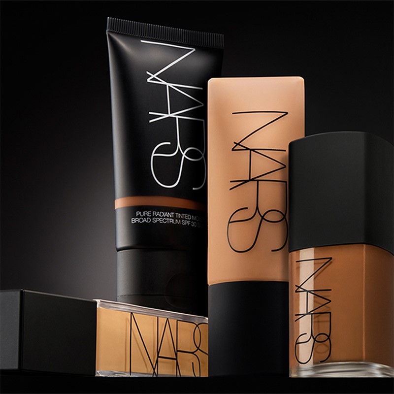 Fyra foundationprodukter i olika nyanser från NARS placerade mot en mörk bakgrund. Alla produkter har NARS-logotypen tryckt vertikalt på förpackningen. Bakgrunden och produkternas design framhäver deras elegans och mångsidighet inom hudvård och makeup.