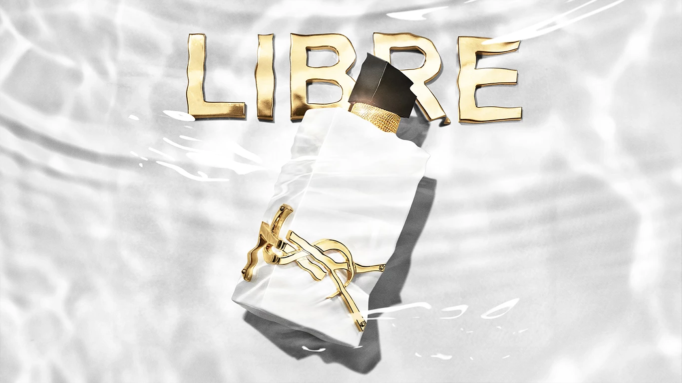 En YSL Libre parfymeflaske ligger under vann. Over flasken står det LIBRE med store gullbokstaver. 
