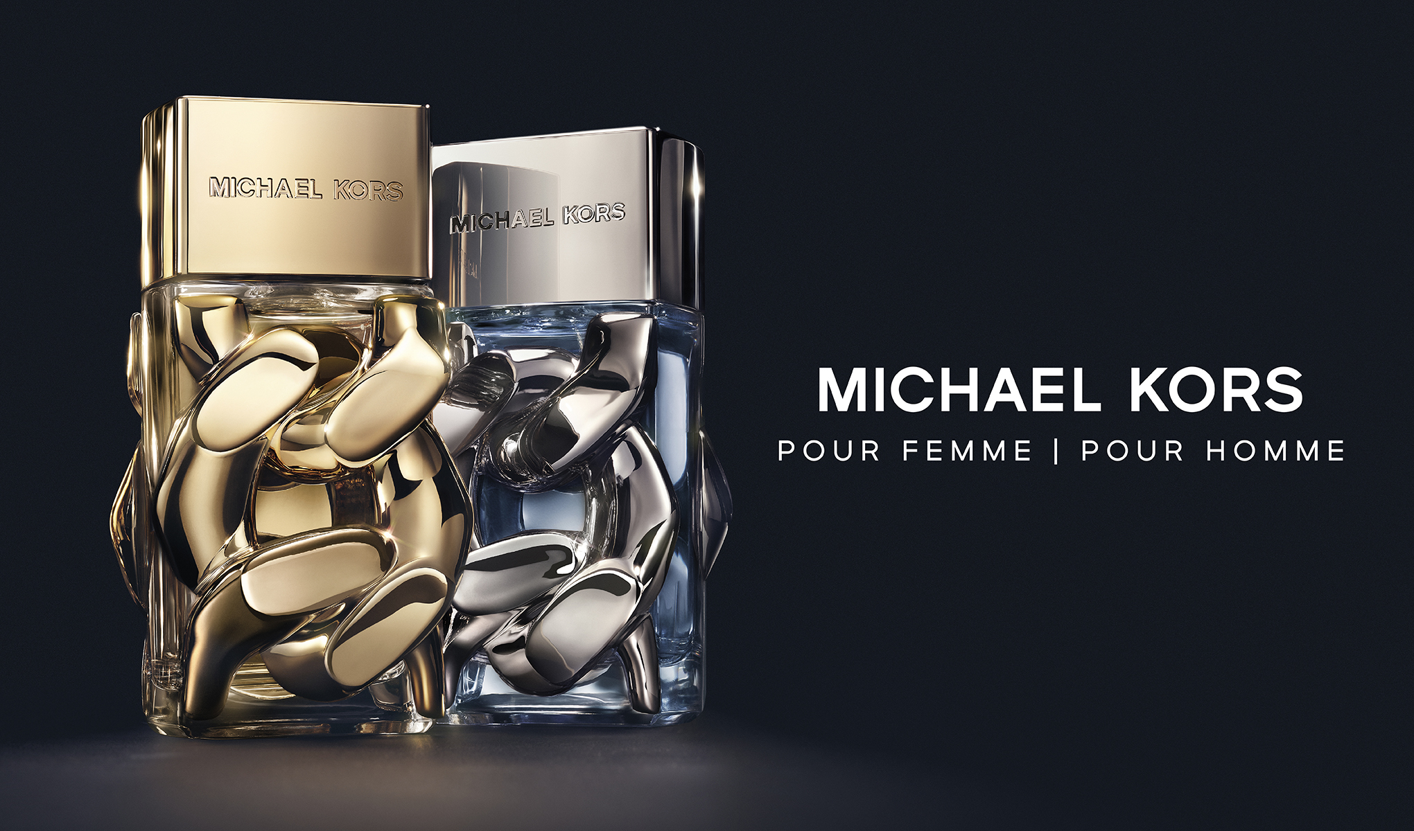 To parfymeflasker fra Michael Kors, en for kvinner og en for menn. Den kvinnelige parfymeflasken er i gull og den mannlige i sølv. Teksten på bildet lyder «Michael Kors Pour Femme | Pour Homme», og bakgrunnen er svart.