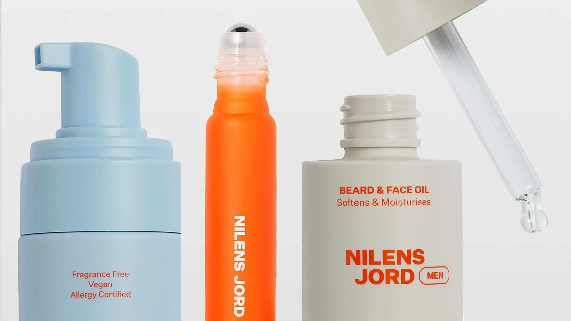 Hudpleie- og groomingprodukter fra Nilens Jord MEN vises mot lys bakgrunn, inkludert skumrens, roll-on og Beard & Face Oil med pipette. Synlig tekst på emballasjen inkluderer “Fragrance Free”, “Vegan”, “Allergy Certified”, “BEARD & FACE OIL Softens & Moisturises” og “NILENS JORD MEN”.