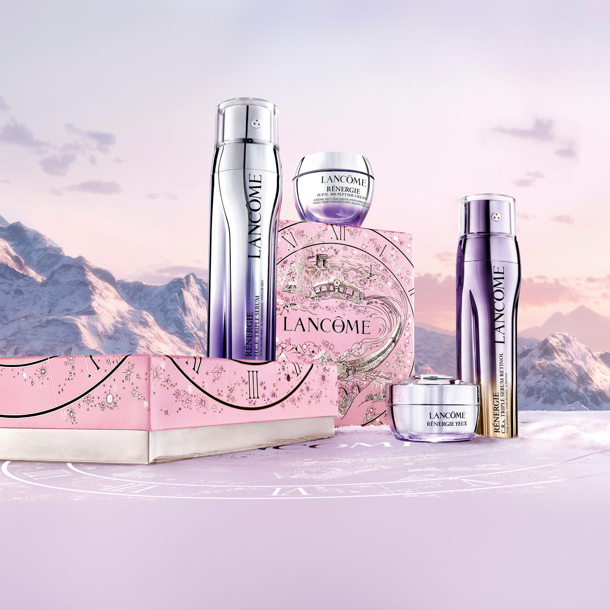 Lancôme Rénergie produktsortiment, inkludert flasker og krukker, plassert på en rosa eske. I bakgrunnen er det et fjellandskap i rosa og lilla toner.
