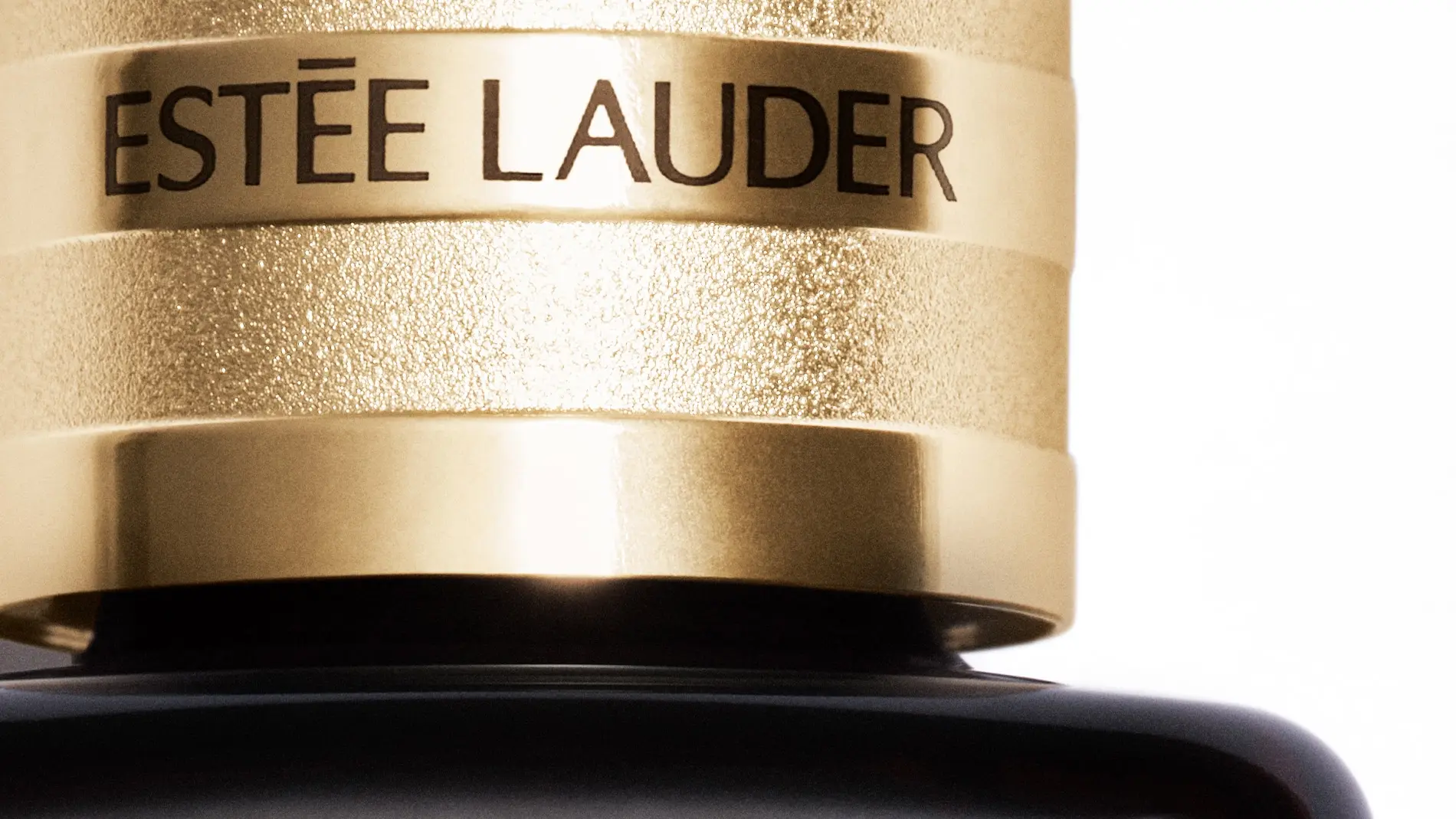 Sort Estée Lauder-produkt i nærbilde, med gullfarget kork, mot en hvit bakgrunn.