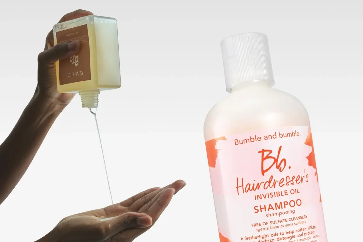 En person häller klar tvättolja i sin hand; bredvid en flaska Bumble and bumble Hairdresser's Invisible Oil Shampoo.