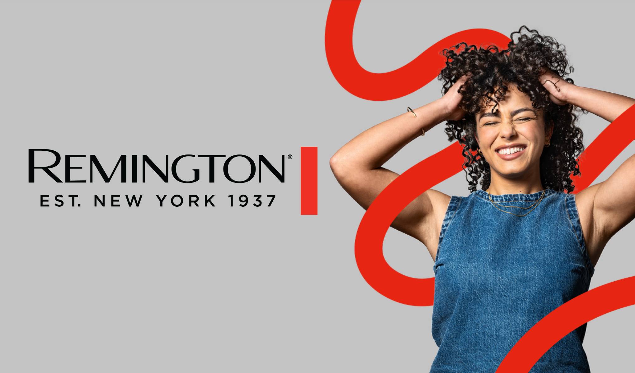 En smilende kvinne tar i det krøllete håret sitt. Ved siden av vises Remington-logoen og teksten “Est. New York 1937”.