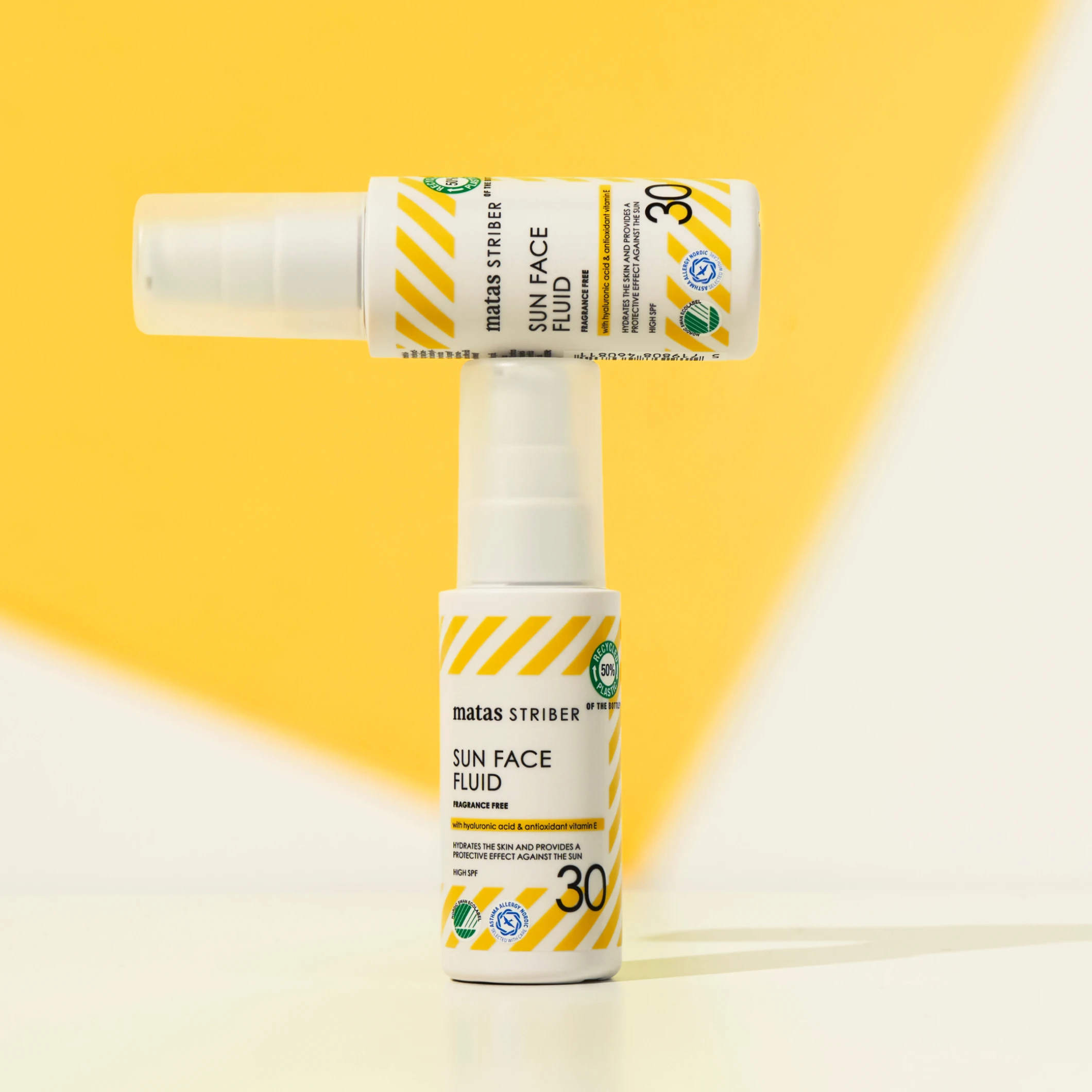 Kaksi Matas Striber Sun Face Fluid SPF 30 -aurinkosuojapulloa, joista toinen on asetettu vaakasuoraan toisen päälle keltaista taustaa vasten.