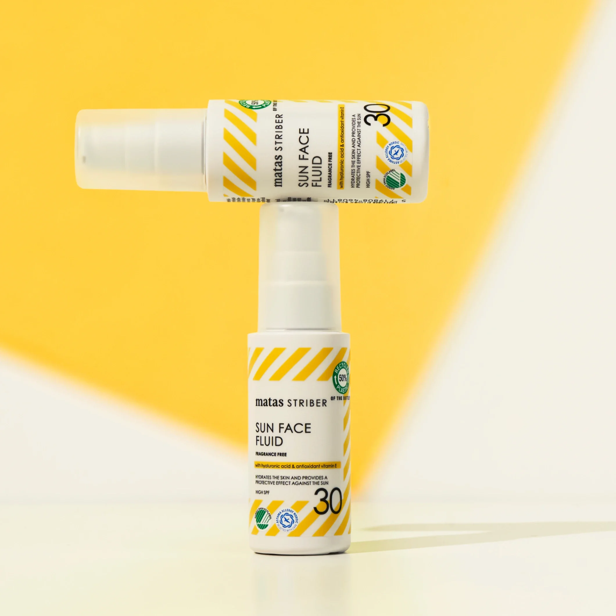 Kaksi Matas Striber Sun Face Fluid SPF 30 -aurinkosuojapulloa, joista toinen on asetettu vaakasuoraan toisen päälle keltaista taustaa vasten.