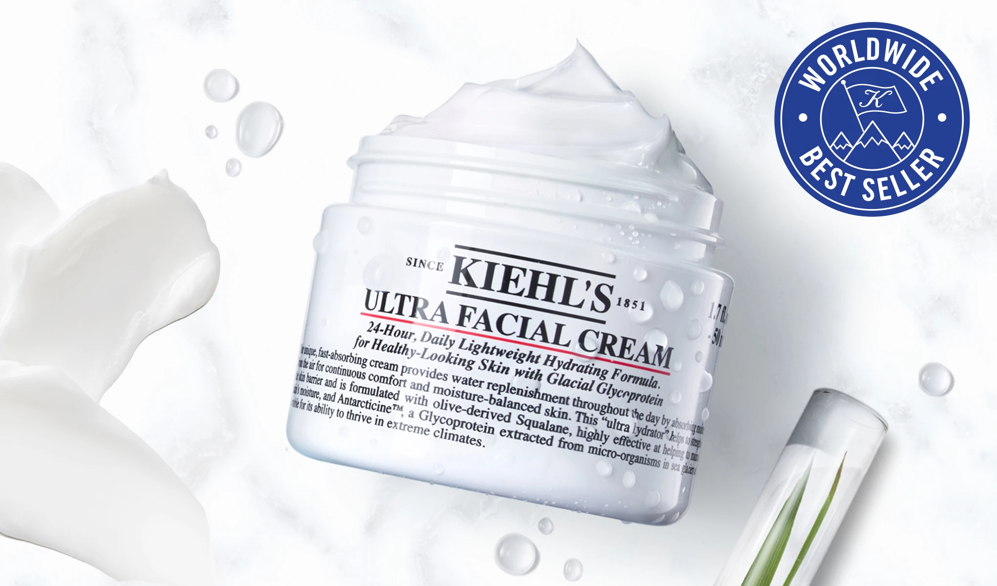En krukke med Kiehl's Ultra Facial Cream med krem som flyter over kanten, plassert mot en hvit bakgrunn. Ved siden av krukken er det en hvit blomst og et reagensrør med en grønn plante. En blå sirkel med teksten «Worldwide Best Seller» er plassert i øvre høyre hjørne.