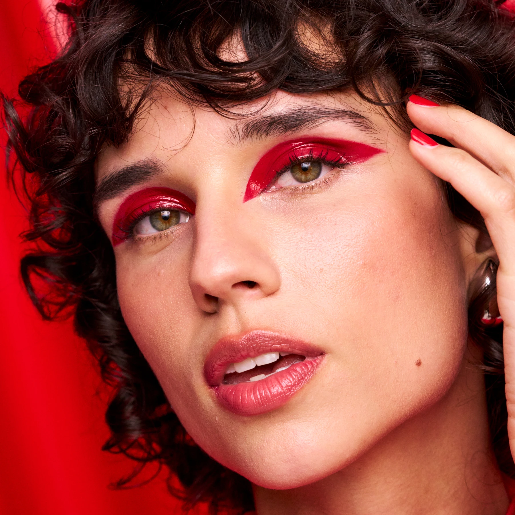 Henkilö koskettaa hiuksiaan punaisella taustalla