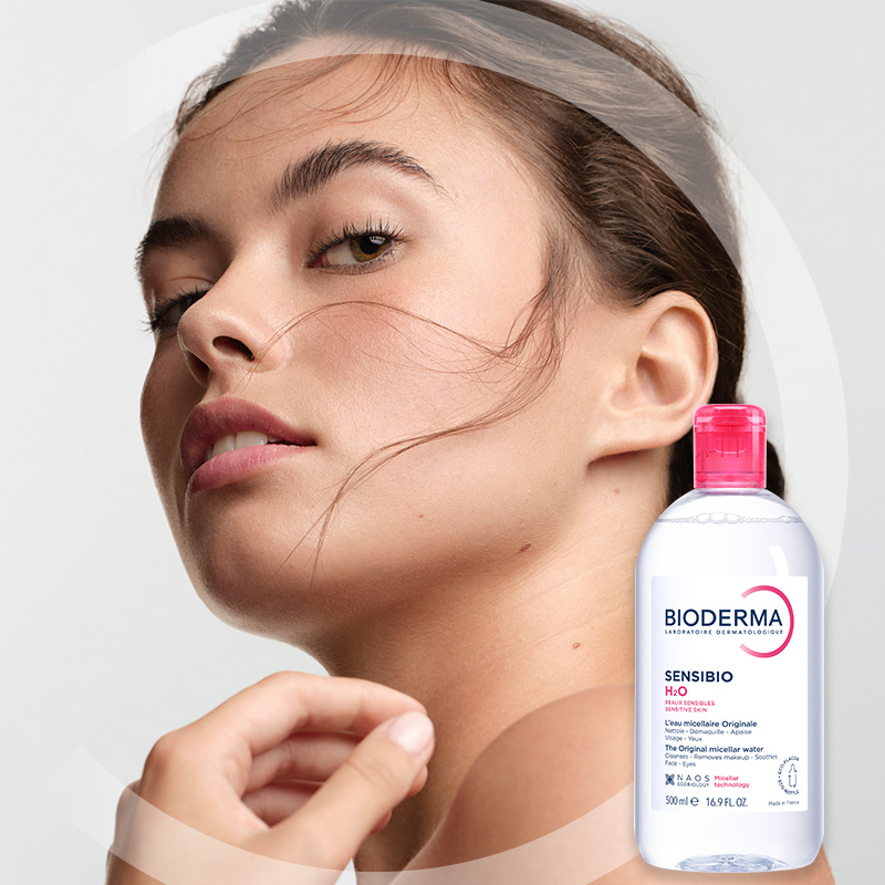En kvinna med frisk hud tittar uppåt. I hörnet visas en flaska Bioderma Sensibio H2O micellärt vatten.