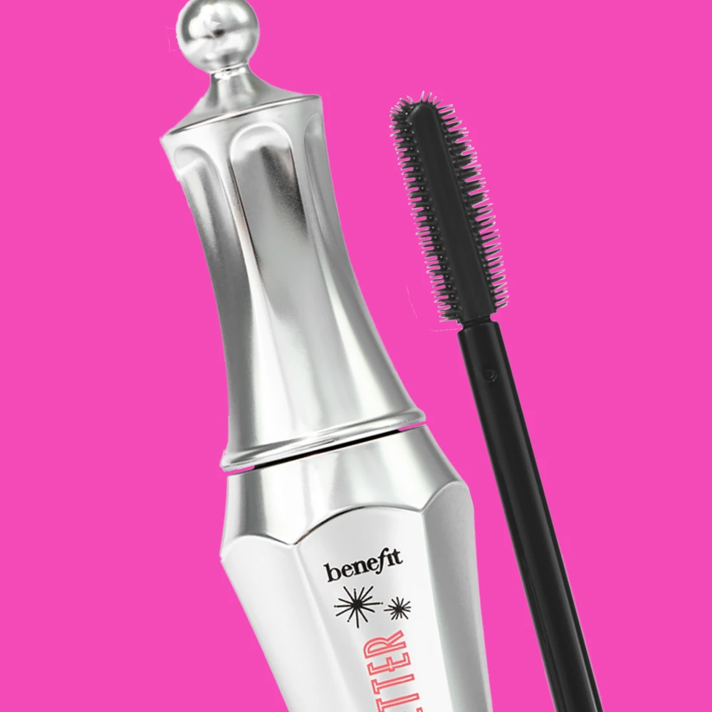 Benefit mascara med silverfärgad kropp och svart borste, mot en rosa bakgrund.
