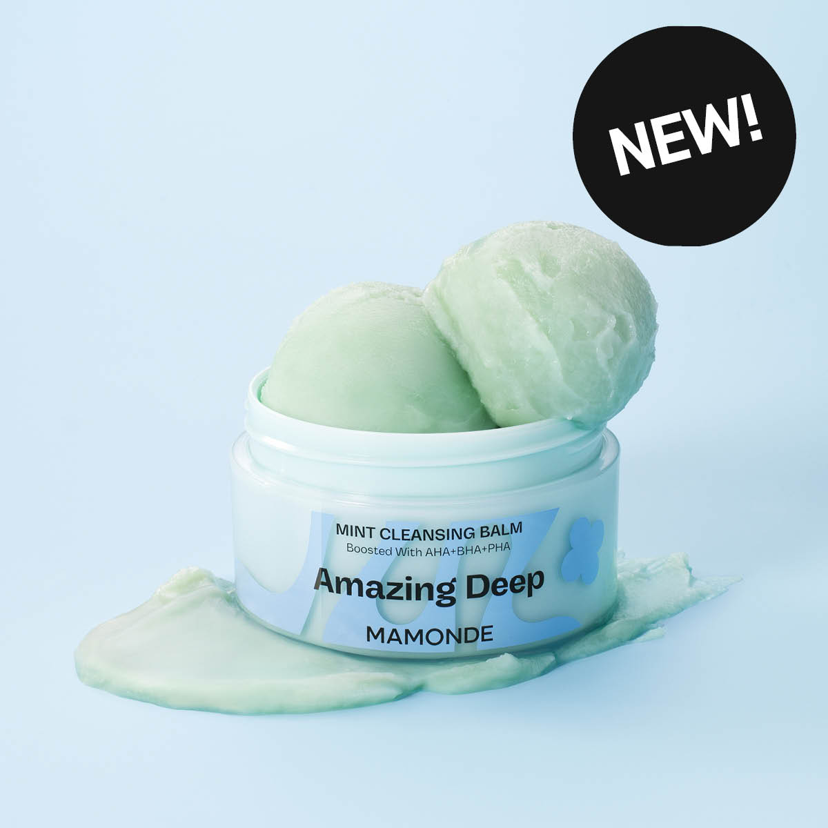 Krukke med rensebalm fra Mamonde med teksten “MINT CLEANSING BALM Boosted With AHA+BHA+PHA” og “Amazing Deep MAMONDE ”. To kuler med grønn balm ligger oppå krukken, og en svart sirkel med teksten “NEW!” vises.