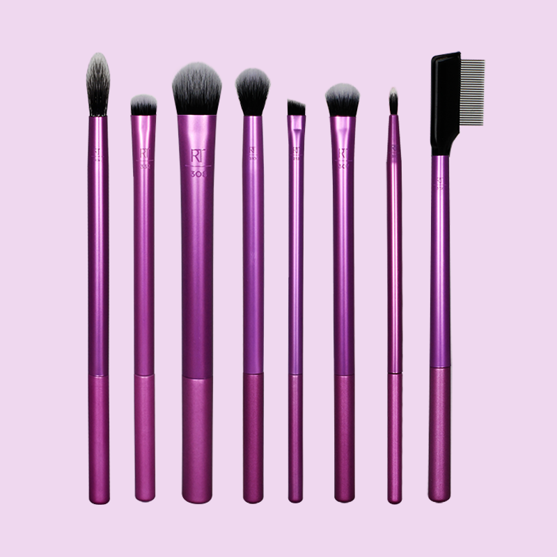 Kahdeksan Real Techniques -meikkisivellintä on järjestetty vaalean violettia taustaa vasten. Siveltimissä on violetit kahvat ja mustat harjakset. 