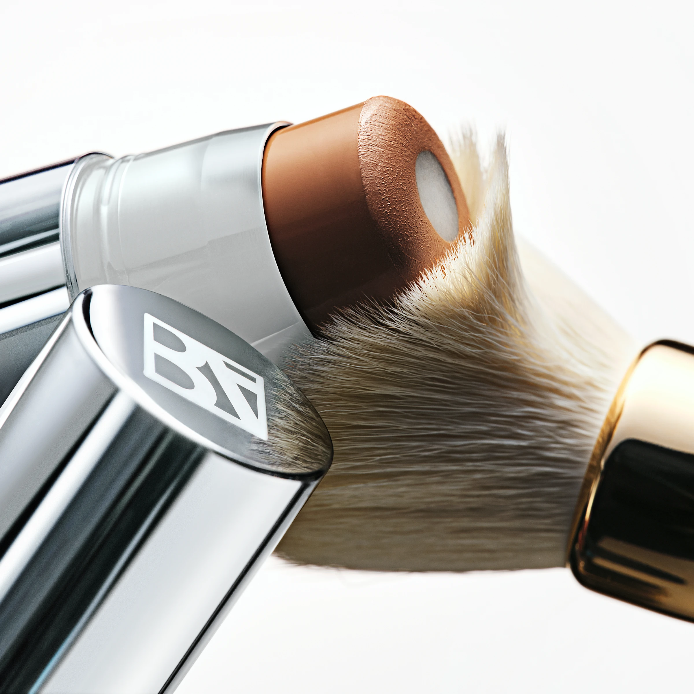 BeautyAct HydraCore Skin Tint Stick i metallforpakning påført mot sminkekost med synlig kremet foundation.