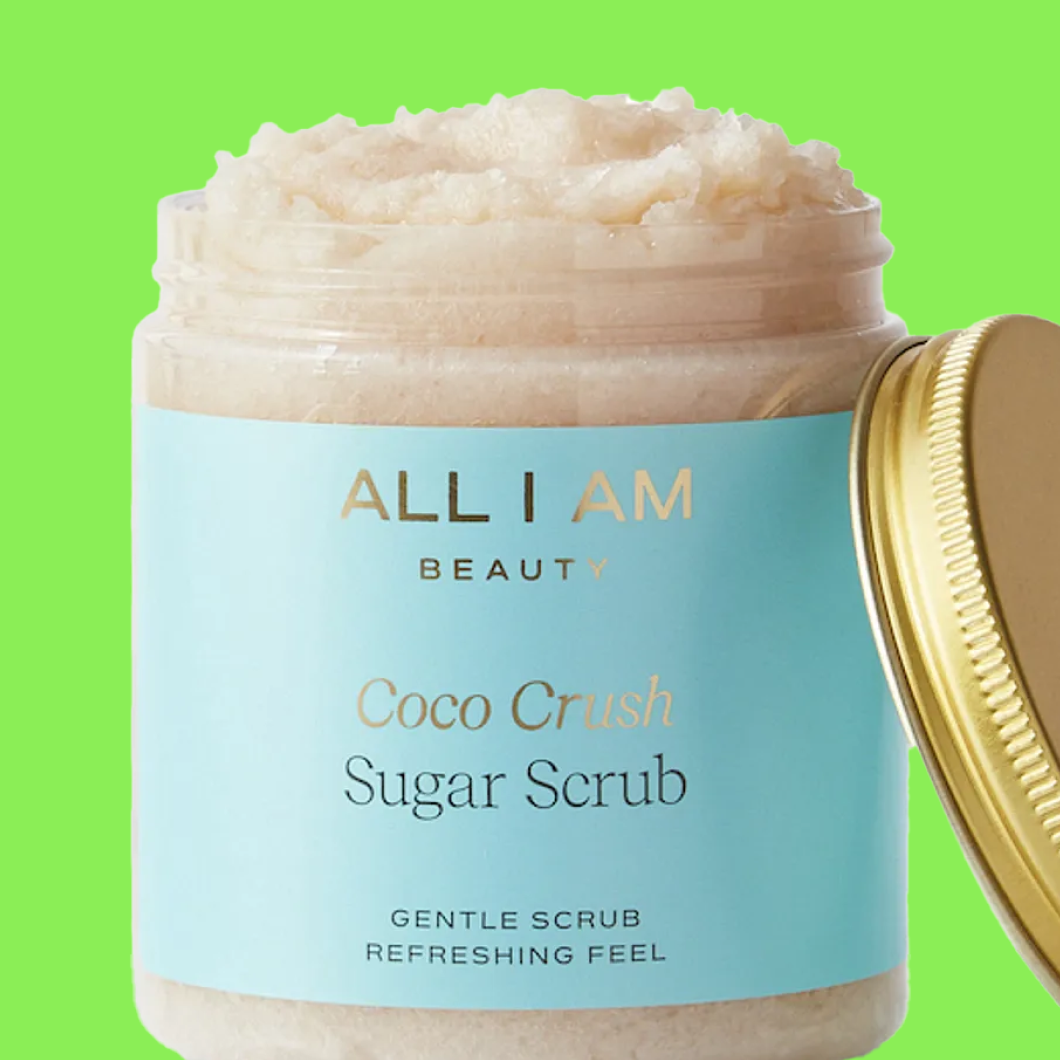 Krukke med kroppsskrubb merket “ALL I AM BEAUTY Coco Crush Sugar Scrub Gentle Scrub Refreshing Feel” med åpent lokk mot grønn bakgrunn.