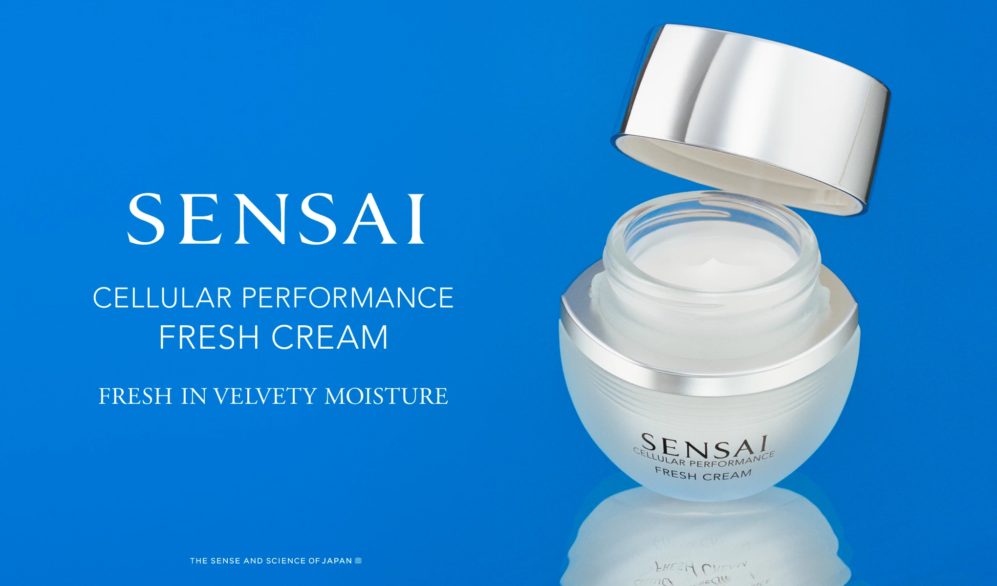 Avoin SENSAI-purkki seisoo sinisellä pinnalla, ja kansi on sen vieressä. Purkin vasemmalla puolella on teksti ”SENSAI Cellular Performance Fresh Cream Fresh In Velvety Moisture”. Alareunassa on pienemmällä tekstillä ”The Sense And Science Of Japan”. Tausta on kirkkaan sininen ja heijastaa purkkia.