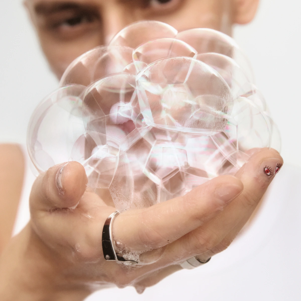 Hand håller genomskinliga såpbubblor, vatten och skum syns runt fingrarna.