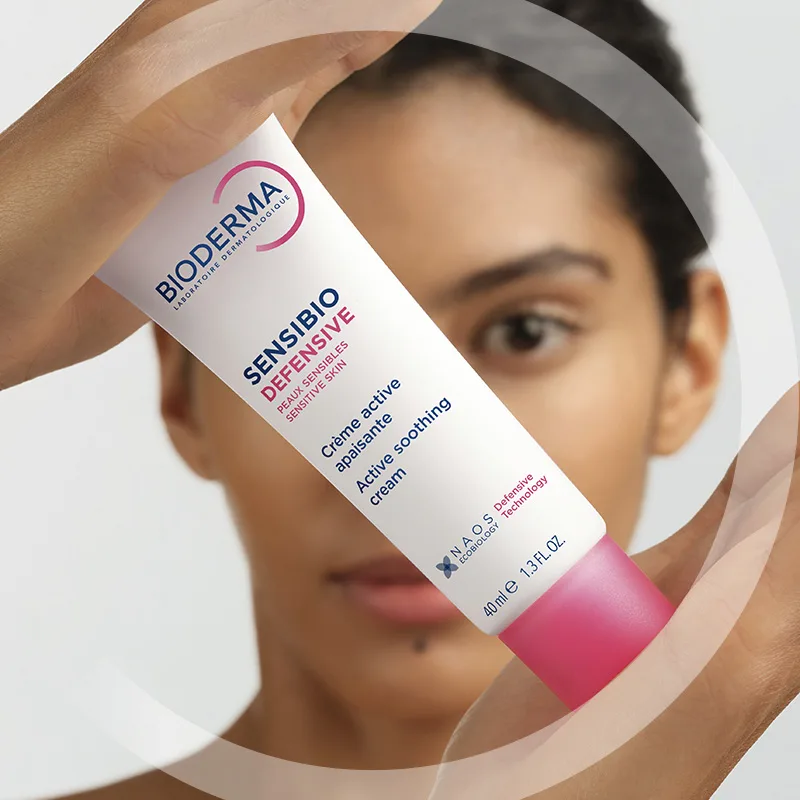 En kvinna håller upp en tub Bioderma Sensibio Defensive ansiktskräm.