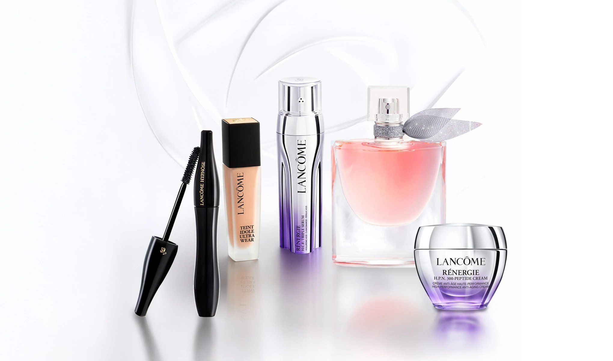 Fem Lancôme-produkter mot lys bakgrunn: mascara med børste, foundation, Rénergie-serum, rosa parfymeflaske og Rénergie-ansiktskrem i krukke.