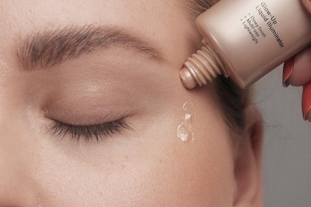 Kvinnas slutna öga med flytande glowy primer som appliceras under det från en flaska.