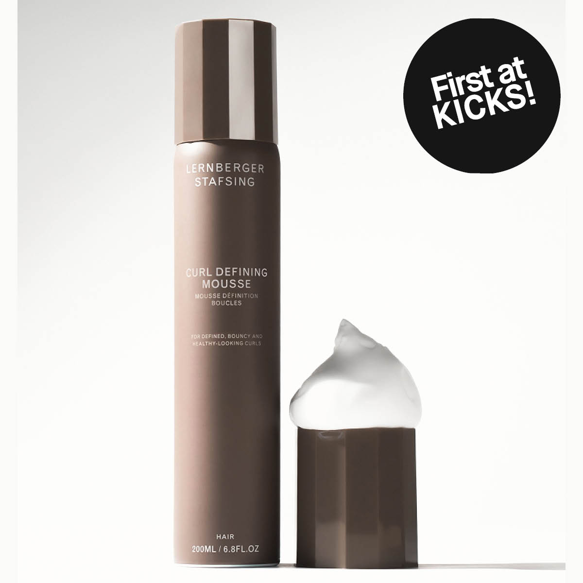 Lernberger Stafsing Curl Defining Mousse i brun flaske med lokk og hvit hårmousse ved siden av, samt en svart sirkel med teksten "First at KICKS!" og produkttekstene "CURL DEFINING MOUSSE", "MOUSSE DÉFINITION BOUCLES", "HAIR 200ML / 6.8FL.OZ".