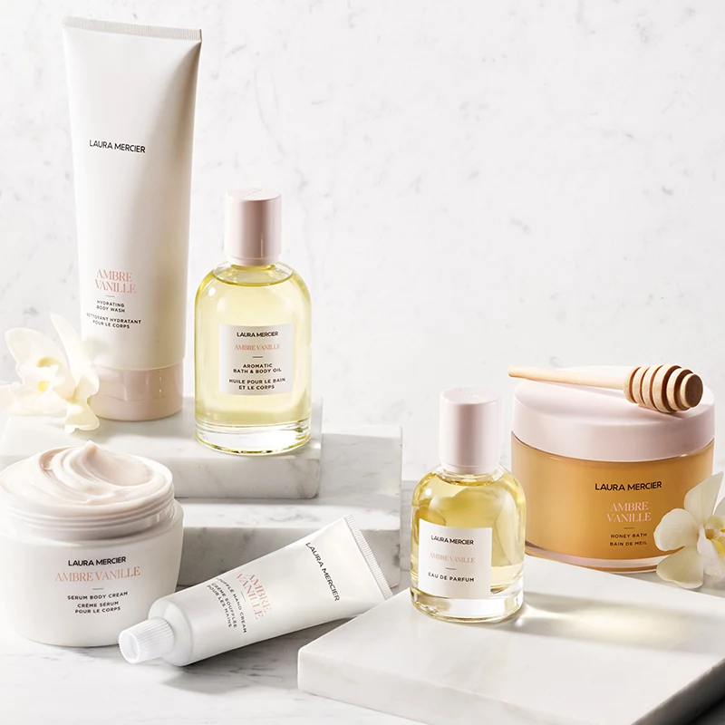 Laura Mercier Ambre Vanille kroppspleieprodukter: kroppsvask, olje, krem og parfyme på marmor med orkideer.