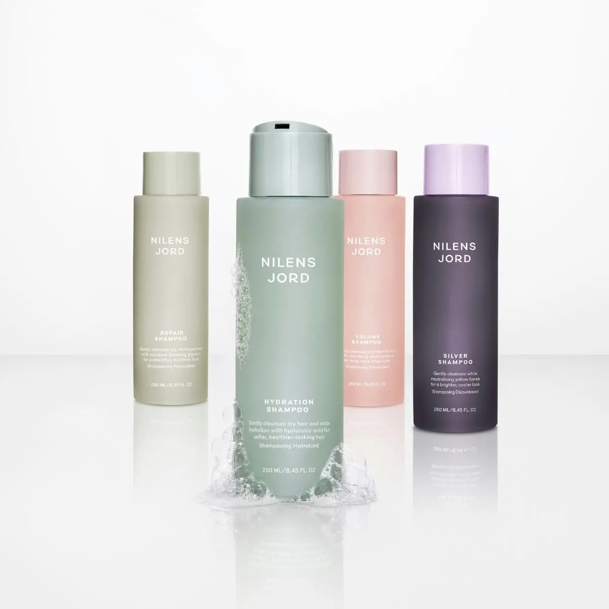 Fire Nilens Jord sjampoflasker: Repair, Hydration, Volume og Silver, med bobler rundt Hydration-flasken.