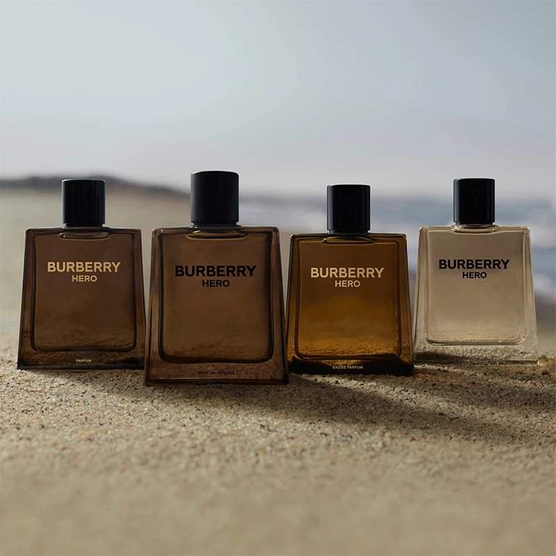 Neljä Burberry Hero -hajuvesipulloa seisoo hiekalla, taustalla näkyy sumuinen maisema.