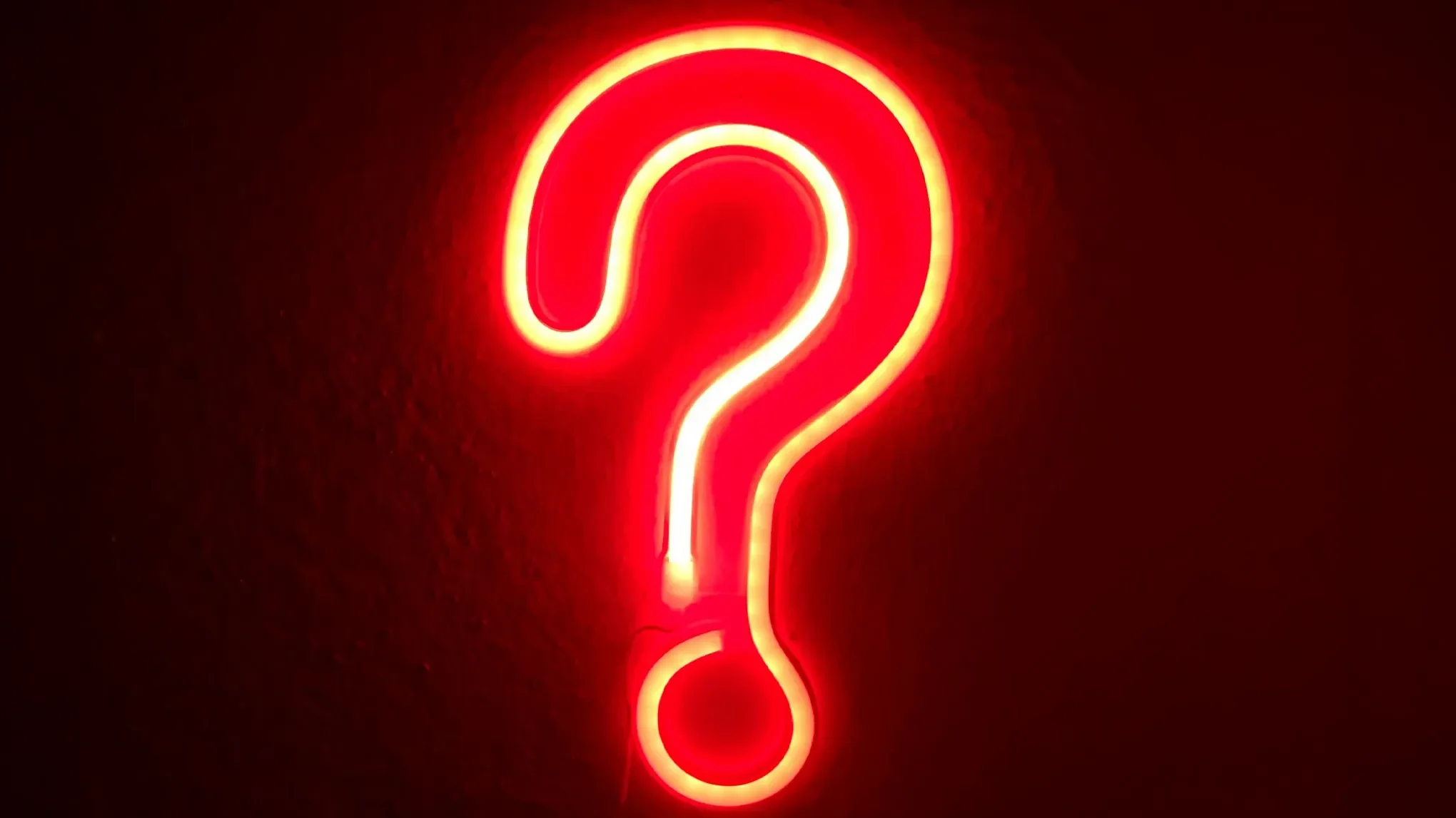 Lysande rött neonskylt i form av ett frågetecken mot mörk bakgrund.