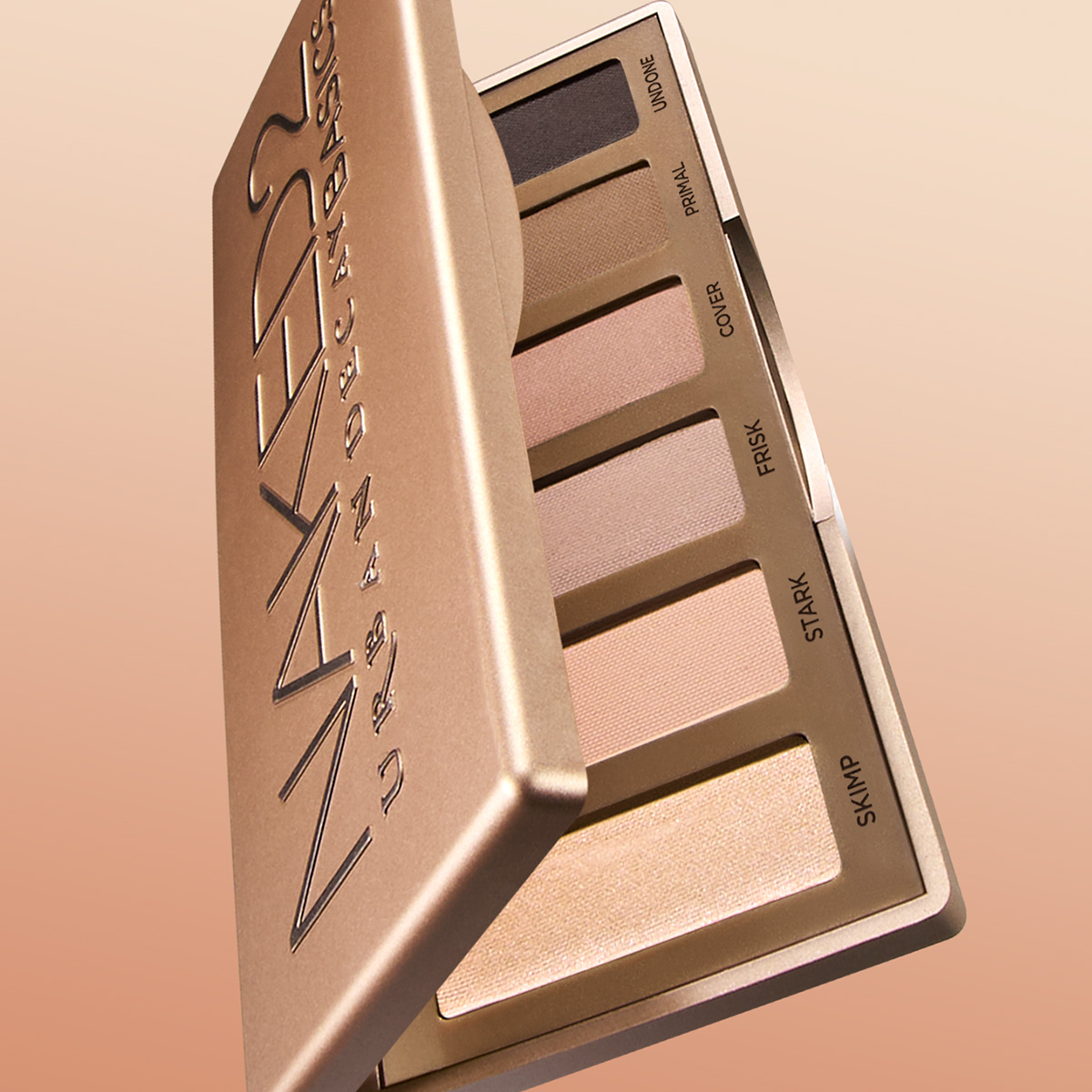 En åpen øyenskyggepalett med seks nøytrale nyanser ligger mot en lys brun bakgrunn. Paletten har teksten "NAKED 2 URBAN DECAY BASICS".