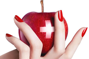 En hand med rödmålade naglar håller i ett rött äpple med en vit korssymbol på. Bakgrunden är vit.