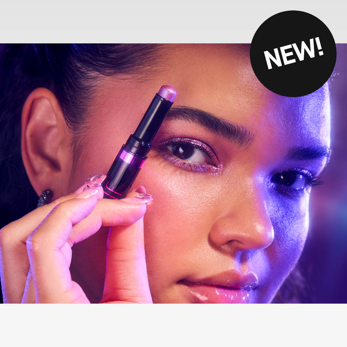 En person håller en ögonskuggspenna och applicerar ögonskugga. Bakgrunden har lila och blå belysning.